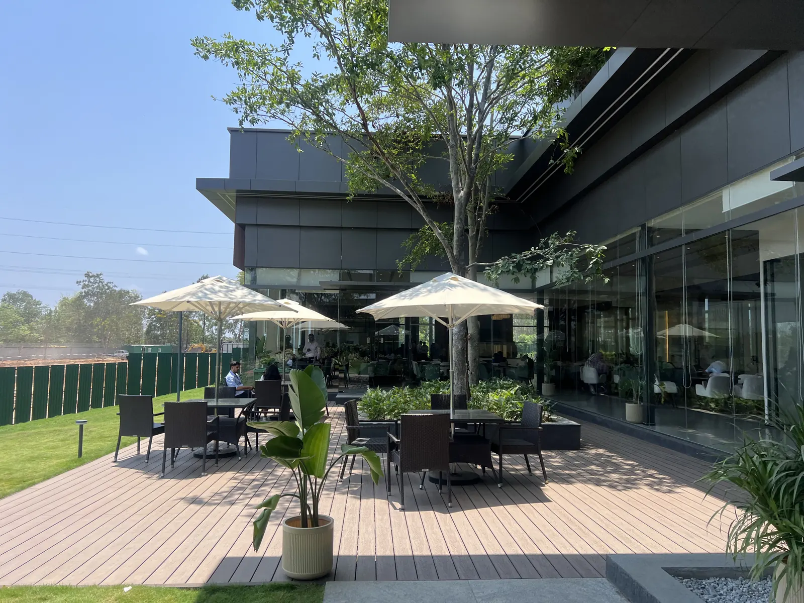 Featured Image of Godrej Vanantara Experience Centre outdoor cafe with timber decking and umbrella seating under mature trees
